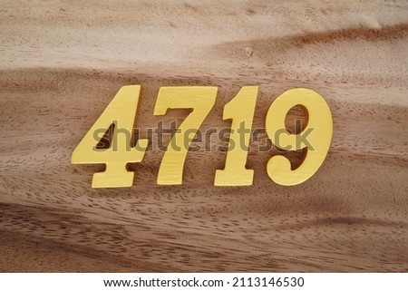 Wooden Arabic numerals 4719 painted in gold on a dark brown and white patterned plank background.