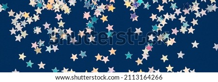 Abstract festive background with holographic sparkling stars confetti on dark blue background. Christmas, New Year or birthday party background for your project. Selective focus, banner