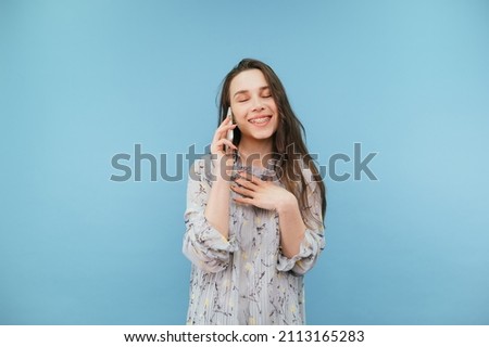 Portrait of happy lady in dress on blue background with smile on face talking on the phone with closed eyes. Isolated.