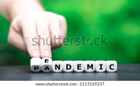 Symbol for a shift from pandemic to endemic. Hand turns dice and changes the word pandemic to endemic. Royalty-Free Stock Photo #2113169237