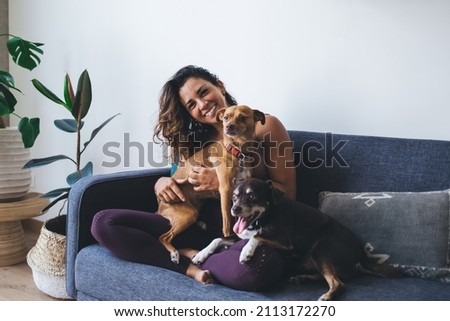 Portrait of happy woman having fun with adorable mongrel dogs spending leisure time in home living room, cheerful female resting at couch with cute doggie pets smiling at camera in apartment Royalty-Free Stock Photo #2113172270