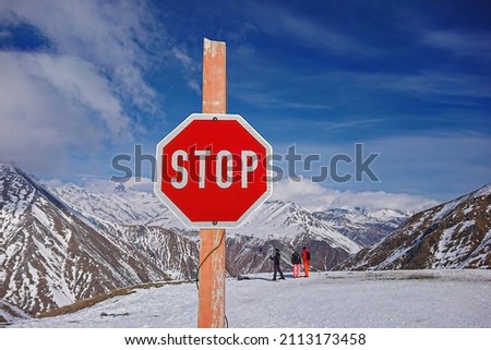 Stop warning signal at ski resort indicating an avalanche or sharp cliff against backdrop of magnificent snowy peaks