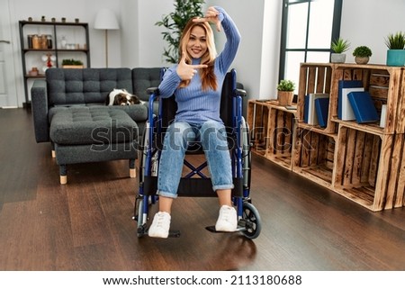 Young beautiful woman sitting on wheelchair at home smiling making frame with hands and fingers with happy face. creativity and photography concept. 