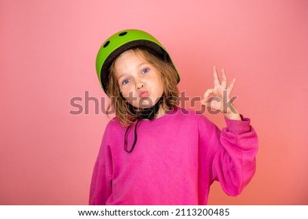 Funny child girl portrait with sign ok isolated on pink background. Kid in safe helmet ready to go on trip. Kindergarten kid protect. Back to go to school. Sport