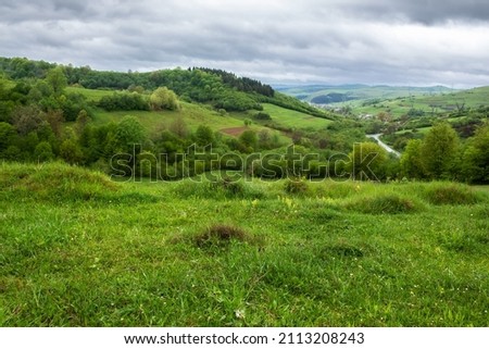 carpathian countryside landscape in spring. grassy meadows, rural fields and forested slopes on hills rolling off in to the distant village in the valley. overcast weather with clouds above the ridge Royalty-Free Stock Photo #2113208243