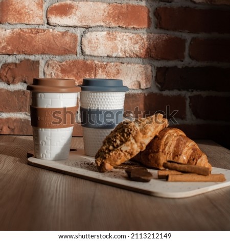 On the table. Breakfast for two. Two cups of hot drink, croissants, cinnamon sticks and dark chocolate.