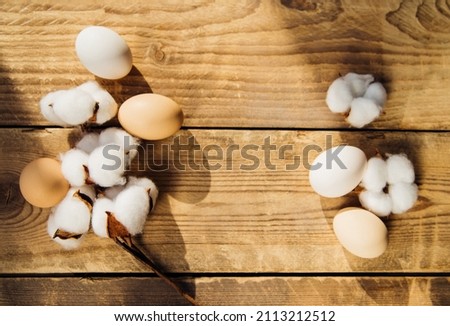 Eggs and a branch with white cotton flowers with sunny shadows on a wooden background. A holiday card. The Concept of the Easter Holiday. Easter decorations.