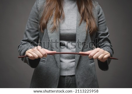 Angry teacher is bending a school pointer stick close up.