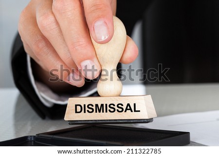 Closeup of hand holding rubber stamp with Dismissal sign at table in office