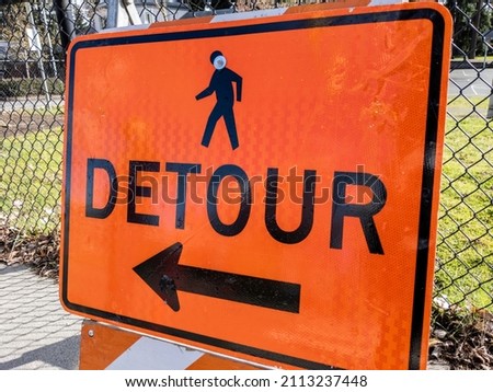 Angled view of an orange detour sign on a sidewalk near a construction site