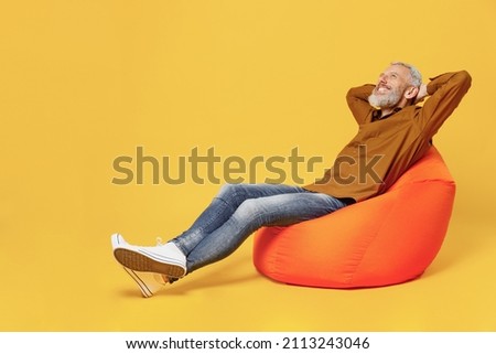 Full size body length happy elderly gray-haired bearded man 40s years old wears brown shirt hands folded under head have rest relax sit in bag chair isolated on plain yellow background studio portrait Royalty-Free Stock Photo #2113243046