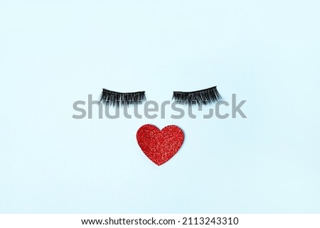 Creative photo of red heart with false eye lashes on blue background