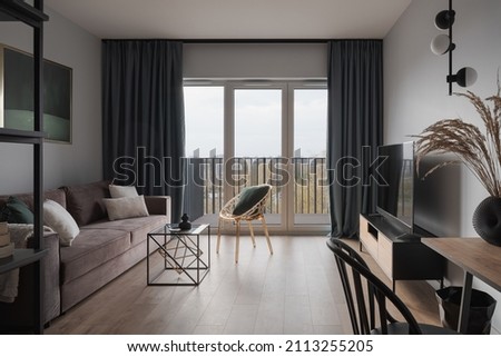 Simple and stylish living room with cozy couch, modern furniture, tv and window doors to balcony Royalty-Free Stock Photo #2113255205