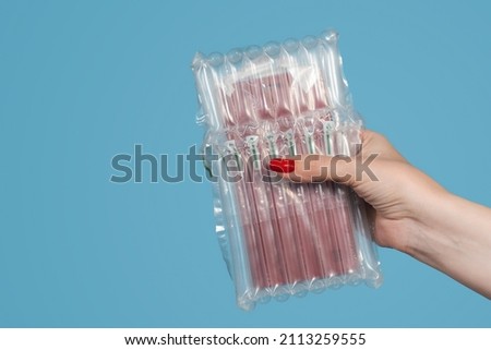 Closeup view stock photography of one manicured female hand holding object packed in bubble plastic protective wrapping isolated on blue wall background
