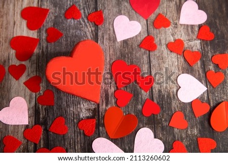 The red and pink paper and felt hearts of different shape and size are on a wooden brown table. The day of Valentine. Copy space