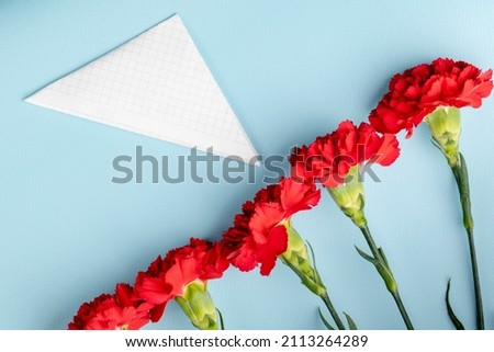 bouquet of red carnations and triangular military envelope field mail symbol with space for text on a blue background, top view, festive background, postcard Defender of the Fatherland Day, May 9