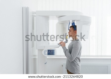 A young man has a computed tomography of the jaw, a circular snapshot of the jaw in modern dentistry. Prevention of caries, prosthetics and dental treatment. Radiology, panoramic scanner. Royalty-Free Stock Photo #2113264820