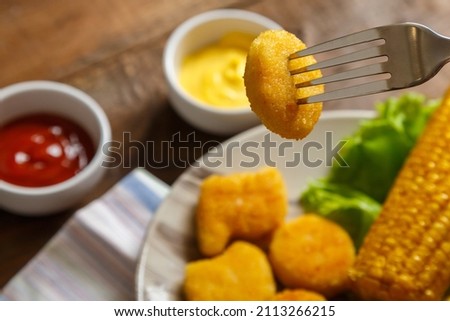 Nuggets, french fries and corn on the cob on lettuce leaves on a plate of nuggets on a pricked fork. Horizontal photo
