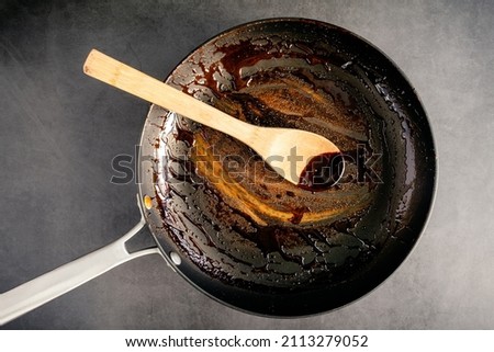 Dirty Nonstick Skillet and Wooden Spoon Used to Make a Balsamic Reduction: An unwashed frying pan and bamboo spoon covered in a sticky glaze