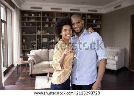 Happy homeowners African couple showing keys from their new apartment house first property, smile look at camera enjoy relocation day pose in living room. Bank loan, mortgage for young family concept Royalty-Free Stock Photo #2113290728