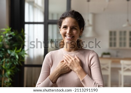 Head shot portrait young attractive Hispanic woman standing alone at home put folded palms on chest feels grateful, express appreciation, sincere feelings smiles looks aside. Believe, charity concept Royalty-Free Stock Photo #2113291190