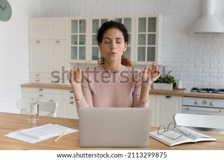Young Hispanic businesswoman sit at table in kitchen near computer closed eyes makes breathing technique calming exercises. Stress management, anxiety relief due business problem. Self-control concept Royalty-Free Stock Photo #2113299875