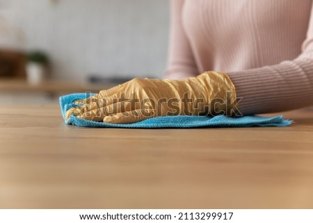 Close up female hand wear rubber latex protective yellow glove cleaning wooden kitchen countertop surface with soft microfiber blue rag. Housekeeping, professional products for cleaning home concept Royalty-Free Stock Photo #2113299917