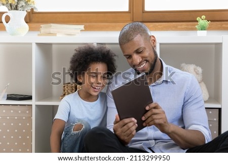African 6s cute little boy and smiling dad enjoy new app, play video games, watching videos vlog on internet, using wireless tablet device. Young generation and modern technology usage, fun concept