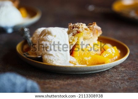 Freshly baked drop biscuit peach cobbler served with French vanilla ice cream over a dark rustic background.