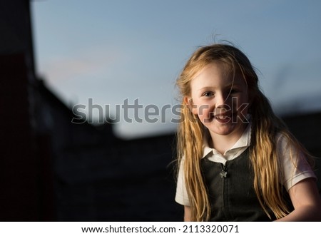 Caucasian young girl looks into camera with a smile, studio light used, outside at evening.