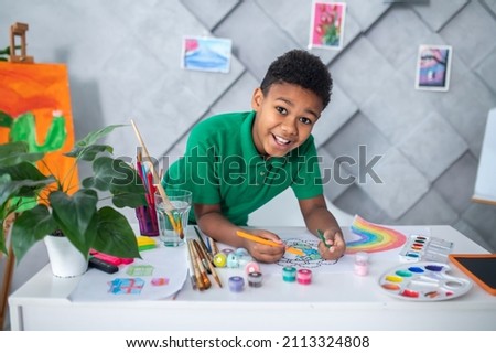 Boy standing at table drawing and looking at camera