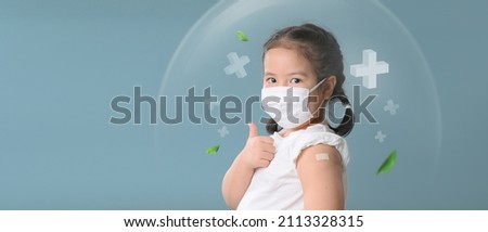 Coronavirus Vaccination Advertisement. Happy Vaccinated Little asian child girl Showing Arm With Plaster Bandage After Covid-19 Vaccine Injection Posing Over Blue Background, Smiling To Camera. Royalty-Free Stock Photo #2113328315