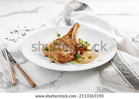 Roasted pork steak with vegetables garnish and sauce. Bone-in ribeye pork chops. Main course of pork in rustic style Royalty-Free Stock Photo #2113363190