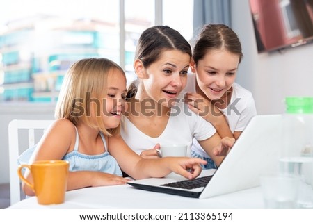 Joyful mom with children watching cartoons on laptop at home