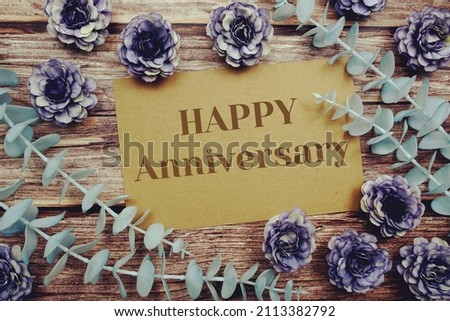 Happy Anniversary typography text on paper card decorate with flower on wooden background Royalty-Free Stock Photo #2113382792