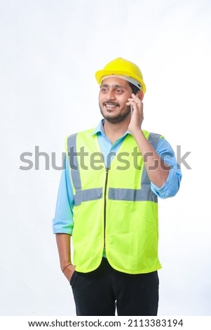 Young indian engineer wearing hardhat and talking smartphone on white background.