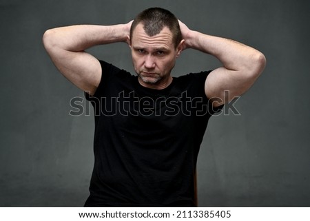 Portrait of an adult caucasian man holding his hands behind his head on a gray background looking at the camera