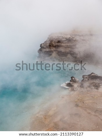A large hot spring in Yellowstone National Park gives off steam above a deep blue steaming pool of hot water due to geothermal volcanic activity Royalty-Free Stock Photo #2113390127