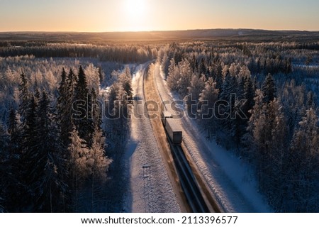 Cargo truck on a highway in winter landscape against sunset. Delivery and transportation in northern europe. Royalty-Free Stock Photo #2113396577