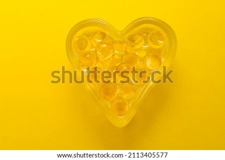 Cod liver oil Omega 3 gel capsules in the form of heart isolated on yellow background. glasses case in the form of heart.