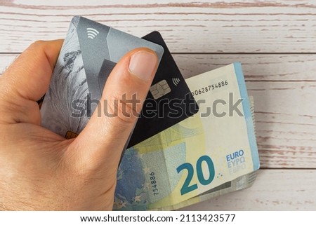 The man's hand holds bank cards with contactless payment, as well as paper euros. Wooden background. Close-up