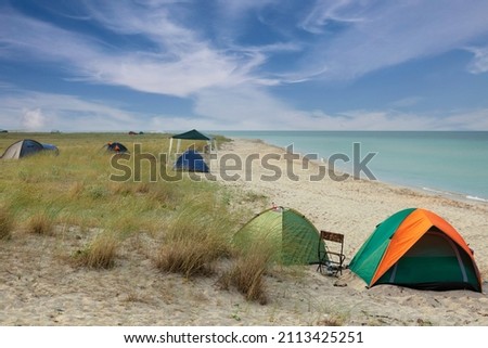 Camping and tourist tent on a wild coast by the sea, early in the morning against a blue sky with clouds. High quality photo