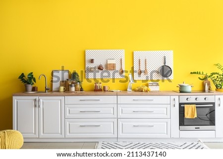 Interior of stylish kitchen with white counters, peg boards and yellow wall Royalty-Free Stock Photo #2113437140
