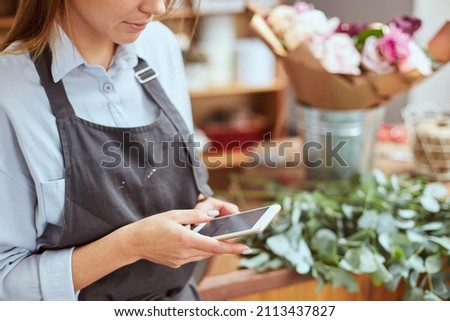 Close up portrait of female florist taking picture of freshly made bouquet on smart phone, creating content for social media. Small local business, self employed, blogger concept