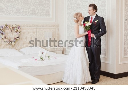 Pretty young couple in elegant wedding clothes tenderly hugging each other in royal room of hotel. Wedding morning of the bride and groom in luxury classic interior. Wedding day ceremony. Young family