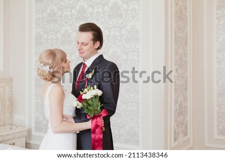 Pretty young couple in elegant wedding clothes tenderly hugging each other in royal room of hotel. Wedding morning of the bride and groom in luxury classic interior. Wedding day ceremony. Young family