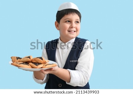 Little Jewish boy with tasty Hamantaschen for Purim holiday on color background