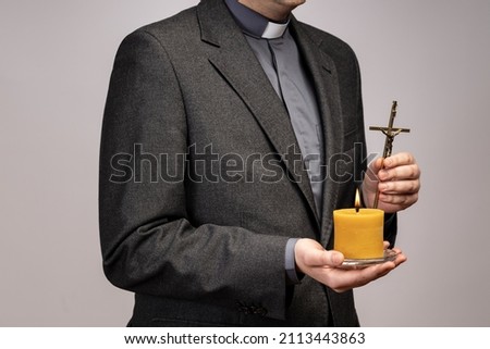 Someone poses on a neutral background. He holds the holy cross and the candle.