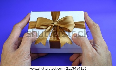 A man's hand holding a gift box. White Gift box with gold ribbon isolated on blue background. Christmas and new year concept, Valentine Concept. High View.