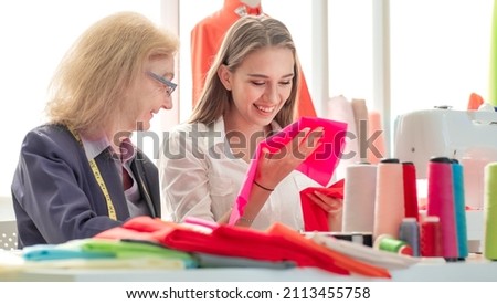 Young beautiful fashion designer and senior dressmaker busy working on fabric color samples in stylish clothing showroom studio. Grandmother and grandchild helping handmade clothes in family business.
